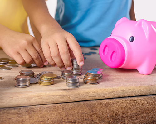 Children stacking coins beside a piggy bank